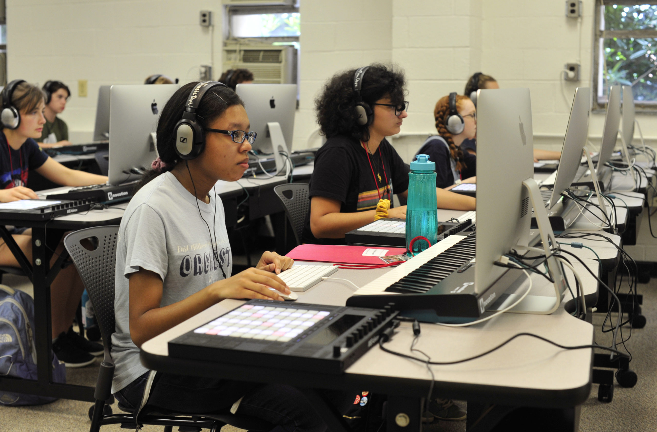 Students wearing headphones work on electronic music compositions in a computer lab equipped with music keyboards and midi controllers.