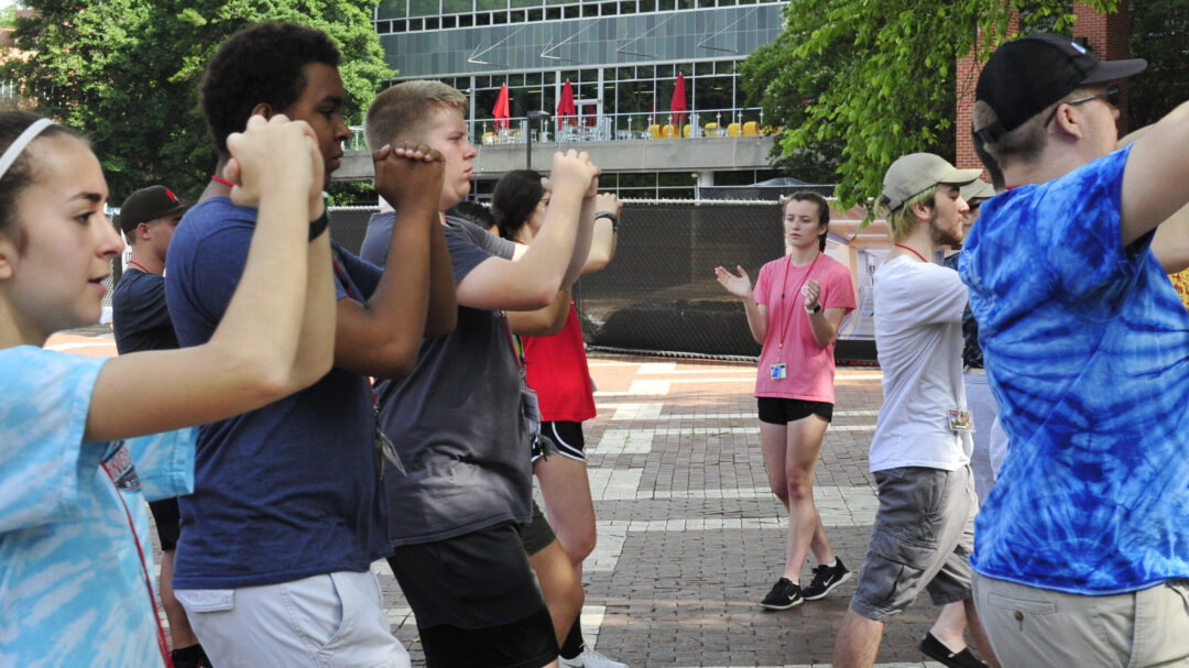 Image of a student practicing conducting while a group of students marches in formation.