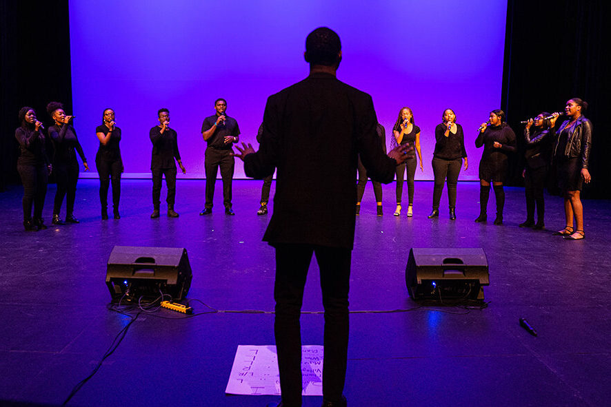 A gospel choir sings with a music director standing in the foreground.