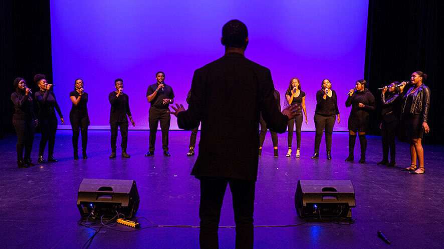 A gospel choir sings with a music director standing in the foreground.