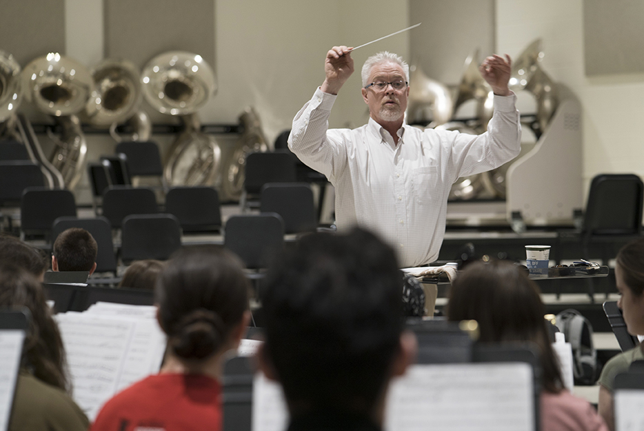 Photograph of Mr. Chris Branam conducting the symphonic band, with students playing instruments in the foreground.