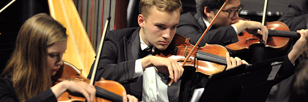 Image of three violin students performing with the symphony.