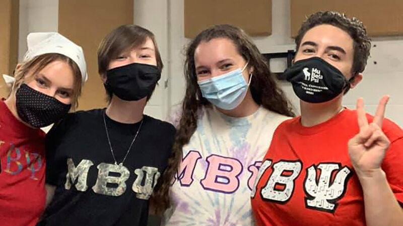 Photo of four students wearing Mu Beta Psi t-shirts and face coverings