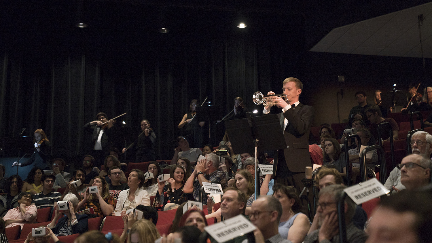 A trumpet player plays surrounded by members of the audience, some of whom are using VR headsets.
