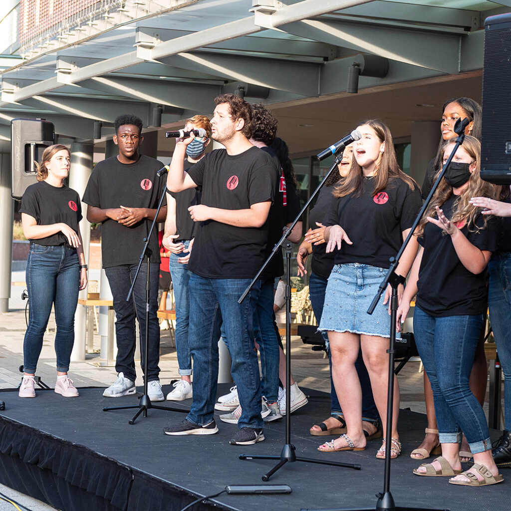 A group of students sing together on an outdoor stage.