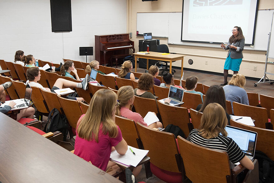 A professor stands at the front of a classroom and lectures to students.