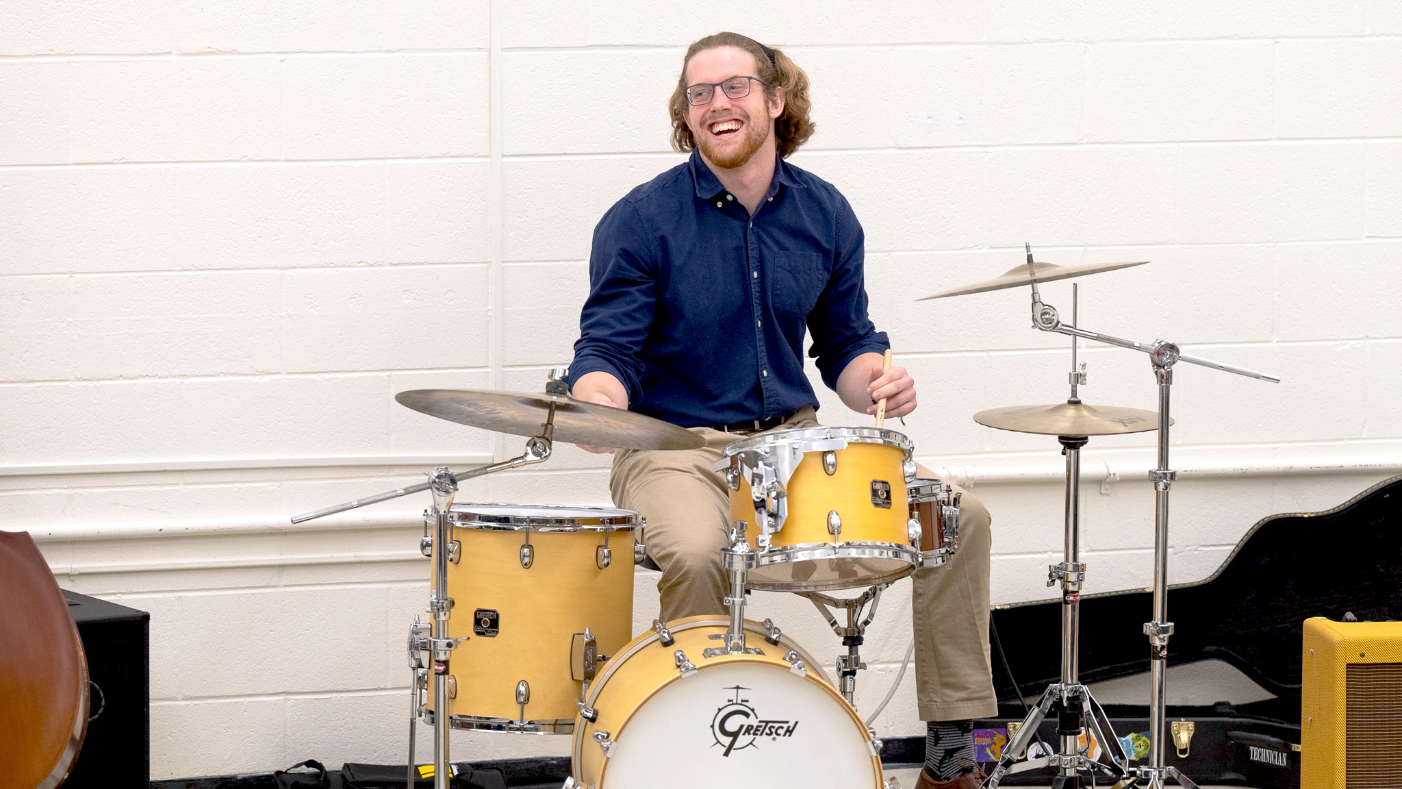a student smiles as he sits at a drum set.
