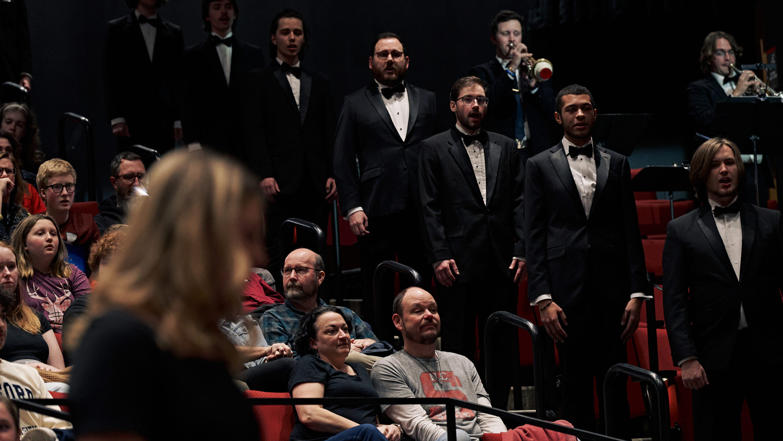 choir and wind ensemble performers stand in the audience as they perform.